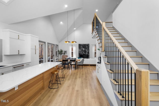 kitchen featuring dishwasher, a high end fireplace, white cabinetry, a kitchen breakfast bar, and hanging light fixtures