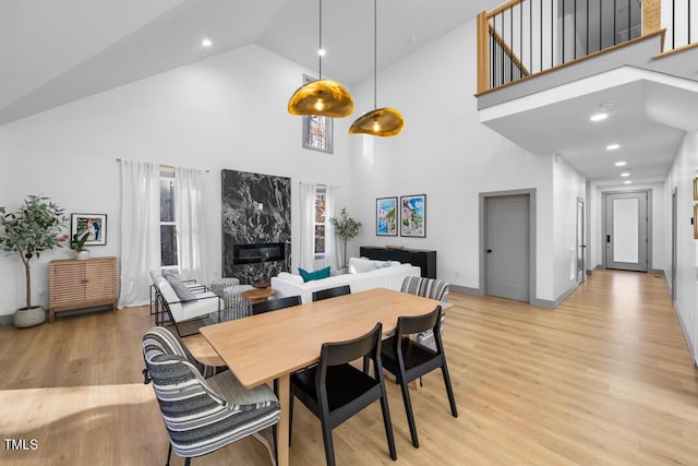 dining space featuring light wood-type flooring, a high end fireplace, and a towering ceiling