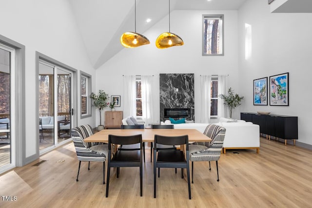 dining room with high vaulted ceiling, a high end fireplace, and light hardwood / wood-style floors