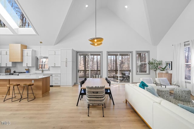 interior space featuring light wood-type flooring, a skylight, a wealth of natural light, and high vaulted ceiling