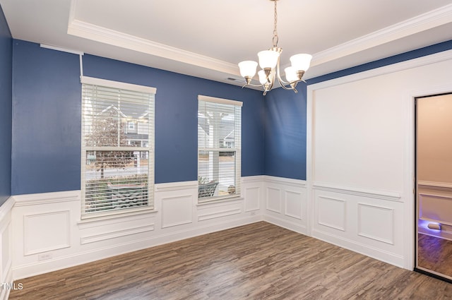 empty room featuring wood-type flooring, a tray ceiling, an inviting chandelier, and crown molding