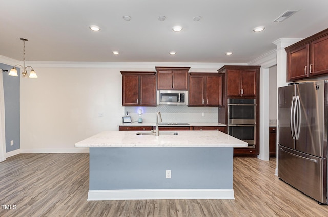 kitchen with a notable chandelier, light stone counters, a kitchen island with sink, and appliances with stainless steel finishes