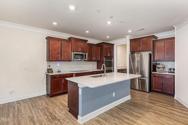 kitchen with a center island with sink, sink, decorative backsplash, light stone countertops, and appliances with stainless steel finishes