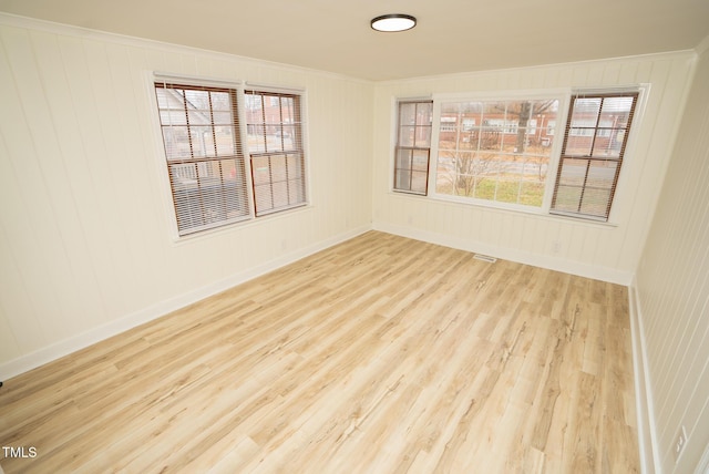 spare room with crown molding, a healthy amount of sunlight, and light wood-type flooring