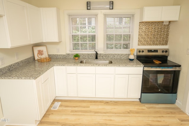 kitchen with light stone counters, white cabinetry, stainless steel range with electric cooktop, and sink