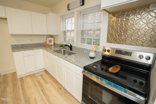 kitchen with light stone countertops, white cabinetry, sink, light hardwood / wood-style floors, and stainless steel range with electric stovetop