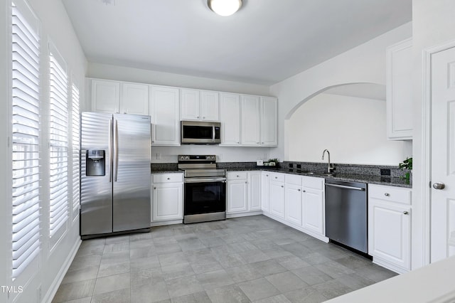 kitchen with stainless steel appliances, sink, dark stone countertops, and white cabinets