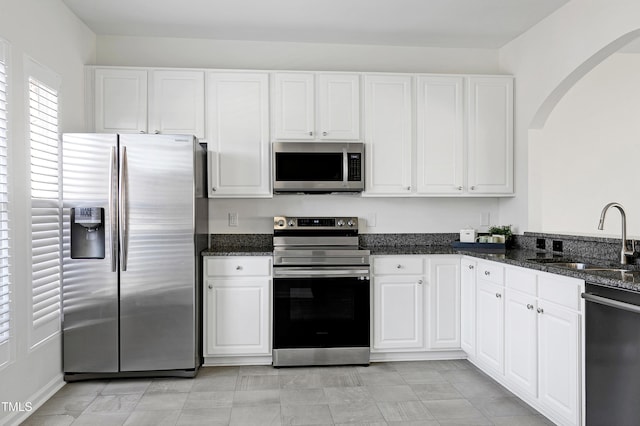 kitchen featuring stainless steel appliances, sink, white cabinets, and dark stone counters