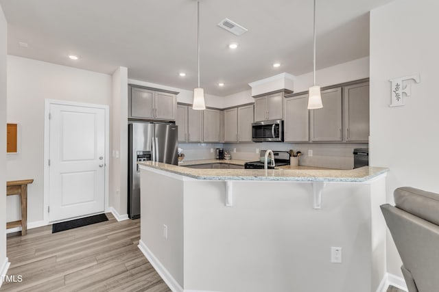 kitchen with pendant lighting, a kitchen bar, kitchen peninsula, and stainless steel appliances