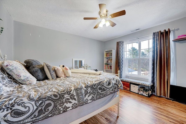 bedroom with ceiling fan, light hardwood / wood-style floors, and a textured ceiling