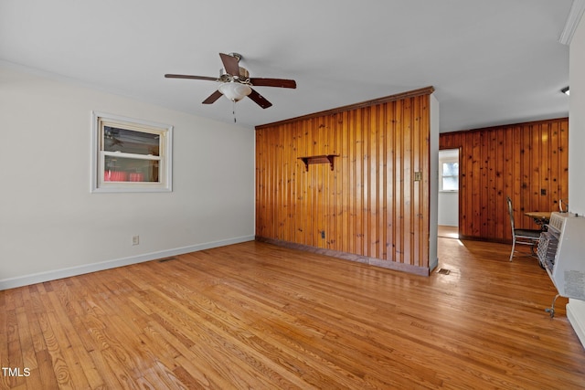 empty room with wood walls, ornamental molding, ceiling fan, and light wood-type flooring