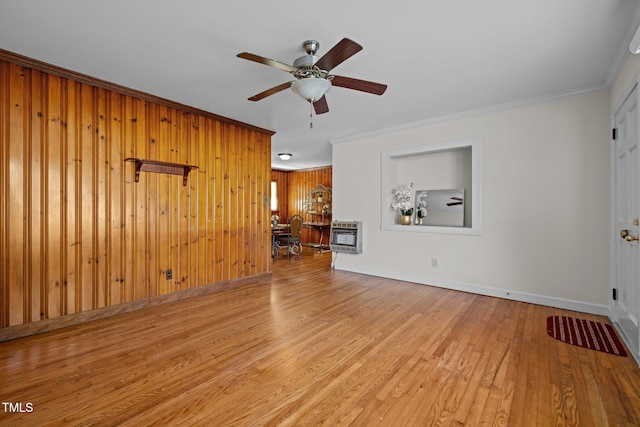 unfurnished living room with wooden walls, light hardwood / wood-style floors, crown molding, heating unit, and ceiling fan