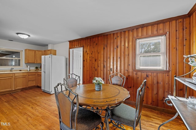 dining room with light wood-type flooring, wooden walls, and sink