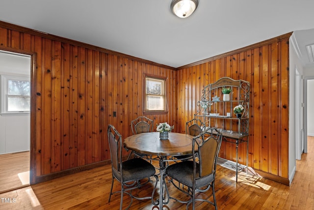 dining room featuring a healthy amount of sunlight, light hardwood / wood-style floors, crown molding, and wood walls