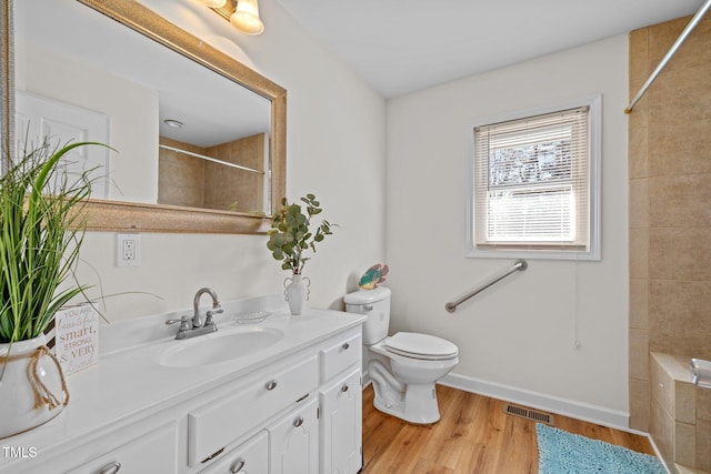 bathroom with a tile shower, vanity, toilet, and hardwood / wood-style floors