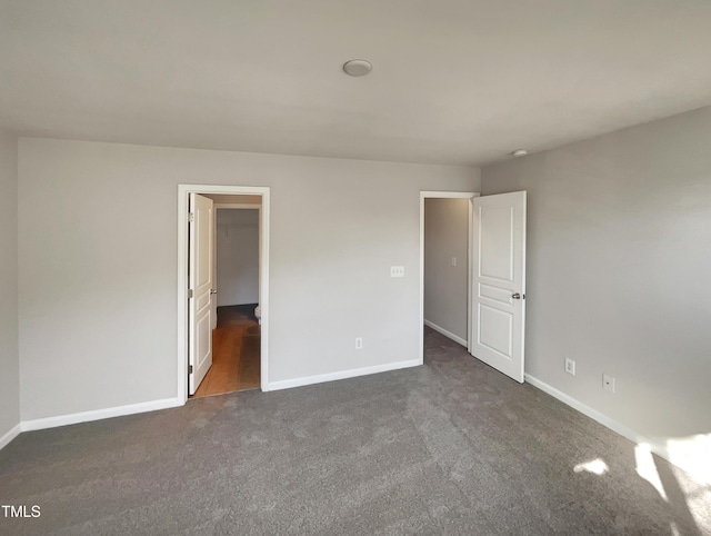 unfurnished bedroom with dark colored carpet and a walk in closet