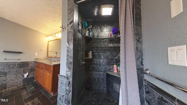 bathroom with vanity, tile patterned floors, tiled shower, a textured ceiling, and tile walls