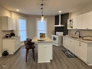 kitchen featuring dark wood-type flooring, a sink, wall chimney range hood, a center island, and gas range gas stove