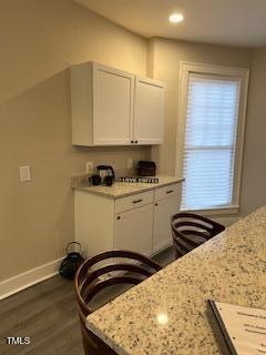 kitchen with dark wood-type flooring, white cabinets, baseboards, and light stone countertops