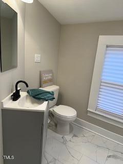 half bathroom with toilet, marble finish floor, baseboards, and vanity