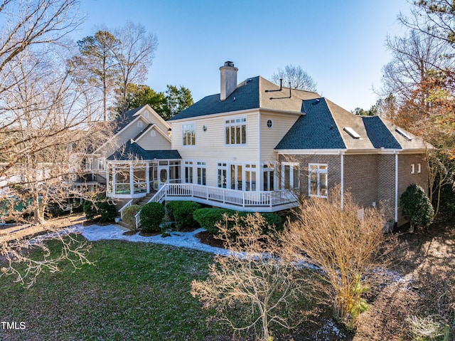 back of house featuring a sunroom, a chimney, roof with shingles, a deck, and a yard