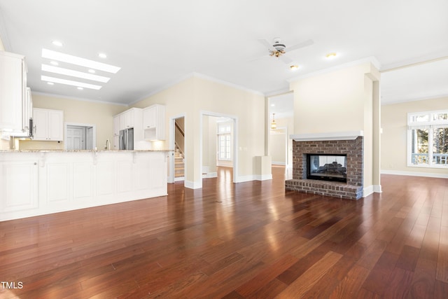 unfurnished living room featuring ornamental molding, a brick fireplace, dark wood finished floors, and baseboards