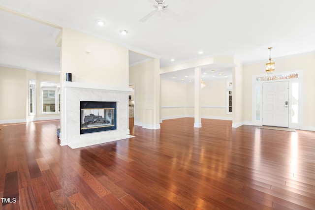 unfurnished living room featuring baseboards, dark wood finished floors, a tile fireplace, ceiling fan, and crown molding