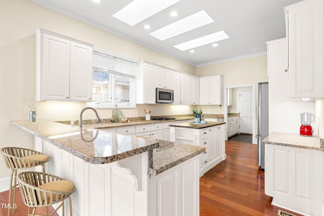 kitchen with stainless steel appliances, a breakfast bar, a peninsula, a skylight, and white cabinetry