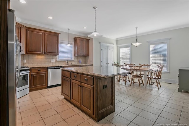 kitchen featuring appliances with stainless steel finishes, decorative light fixtures, a kitchen island, and crown molding