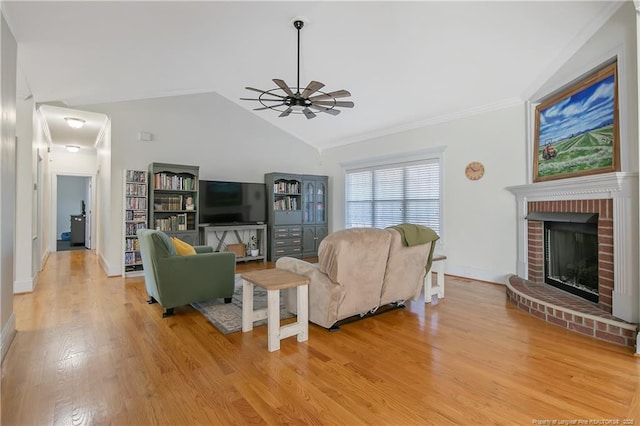 living room featuring light wood-type flooring, ornamental molding, vaulted ceiling, ceiling fan, and a fireplace