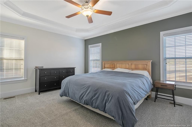 carpeted bedroom featuring ceiling fan, crown molding, multiple windows, and a tray ceiling