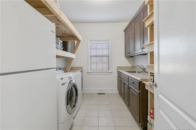 clothes washing area featuring cabinets, light tile patterned floors, sink, and washing machine and clothes dryer