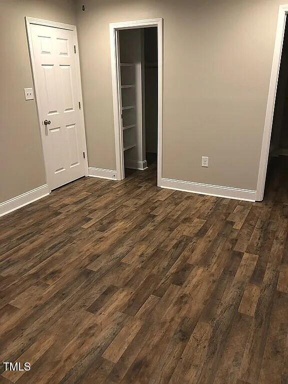 unfurnished bedroom featuring a walk in closet, dark wood-type flooring, and a closet