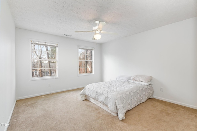 bedroom with ceiling fan, light colored carpet, and a textured ceiling