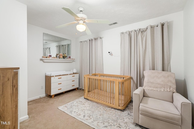 bedroom with light carpet, a nursery area, and ceiling fan