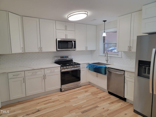 kitchen featuring appliances with stainless steel finishes, tasteful backsplash, pendant lighting, light hardwood / wood-style floors, and white cabinetry