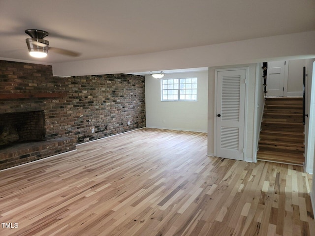 unfurnished living room with light wood-type flooring, a fireplace, and brick wall