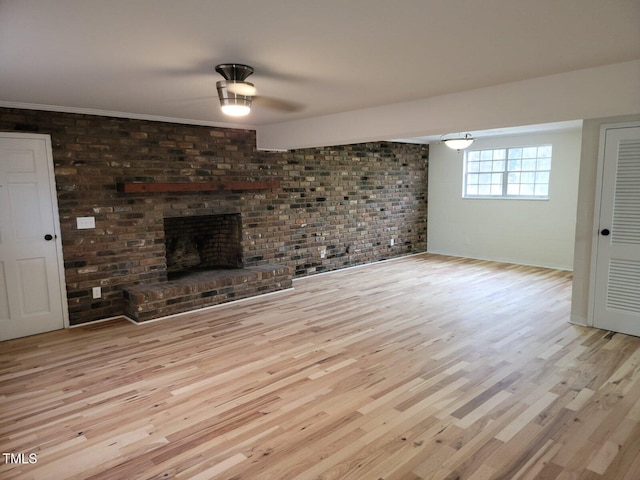 unfurnished living room featuring crown molding, a fireplace, brick wall, and light wood-type flooring