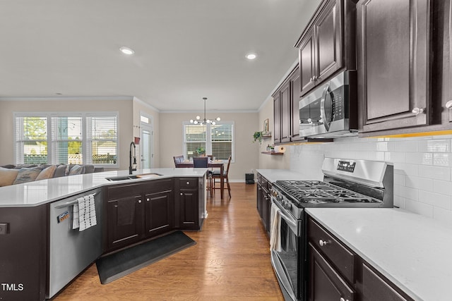 kitchen with sink, appliances with stainless steel finishes, hanging light fixtures, ornamental molding, and light wood-type flooring