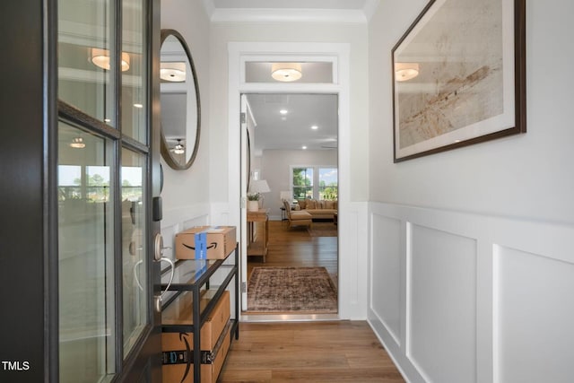 hall featuring a wainscoted wall, ornamental molding, a decorative wall, and wood finished floors