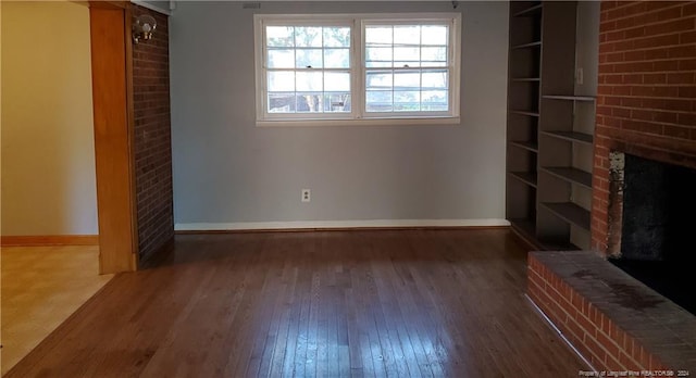 unfurnished living room with dark wood-type flooring and a brick fireplace