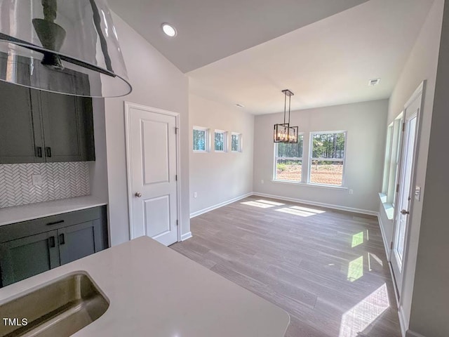 kitchen featuring light wood-type flooring, backsplash, pendant lighting, a chandelier, and lofted ceiling