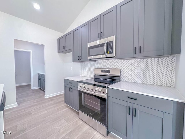 kitchen with backsplash, stainless steel appliances, light hardwood / wood-style flooring, gray cabinets, and lofted ceiling