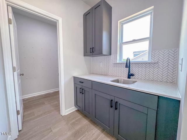 kitchen with backsplash, gray cabinets, sink, and light hardwood / wood-style flooring