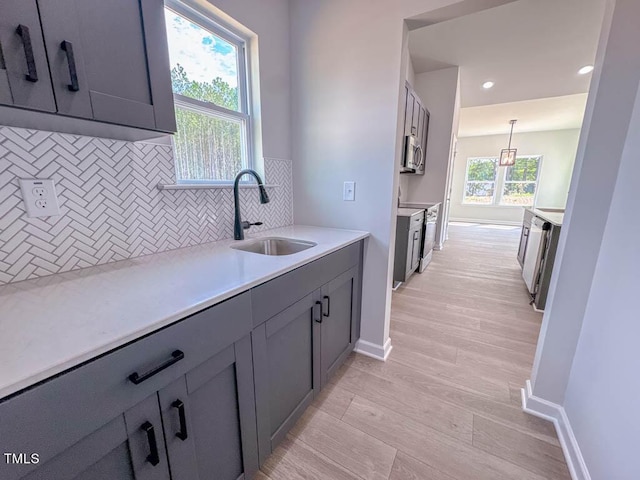 kitchen featuring appliances with stainless steel finishes, backsplash, sink, gray cabinets, and hanging light fixtures