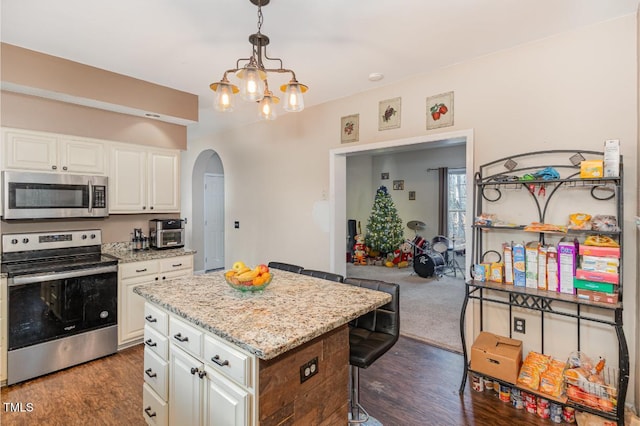 kitchen with a center island, hanging light fixtures, appliances with stainless steel finishes, light stone counters, and white cabinetry