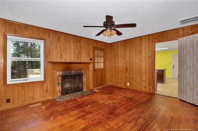 unfurnished living room featuring a fireplace, hardwood / wood-style floors, ceiling fan, and wooden walls