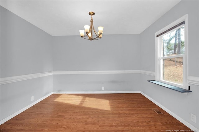 spare room featuring wood-type flooring and an inviting chandelier