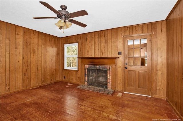 unfurnished living room with ceiling fan, a fireplace, wood walls, and dark hardwood / wood-style floors