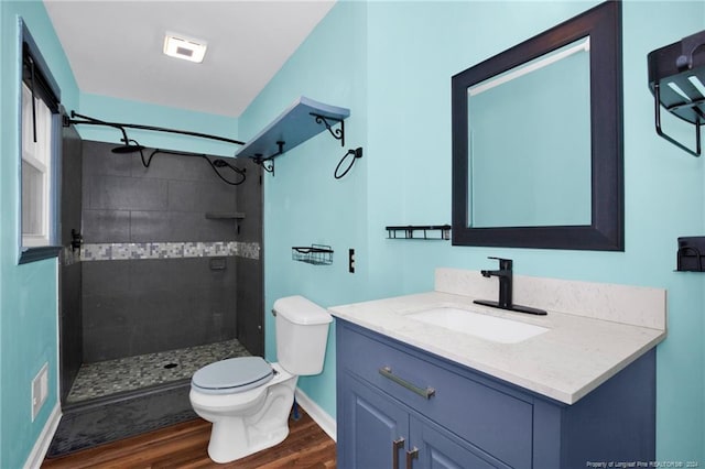 bathroom with hardwood / wood-style floors, vanity, a tile shower, and toilet